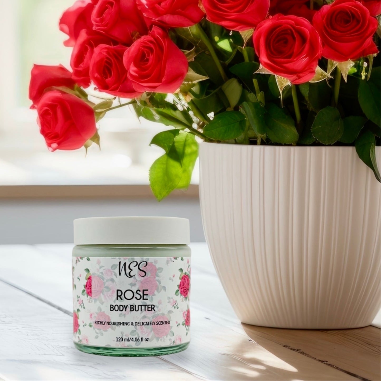 NES Rose Body Butter beside fresh red roses on a sunny windowsill