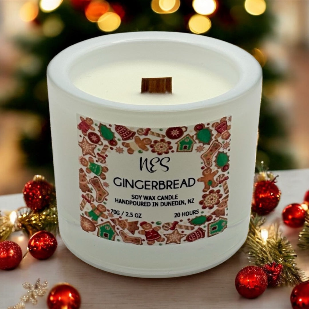 Gingerbread candle with decorative label on a table with Christmas decorations and blurred tree in the background. Handpoured in Dunedin, NZ by NES soap