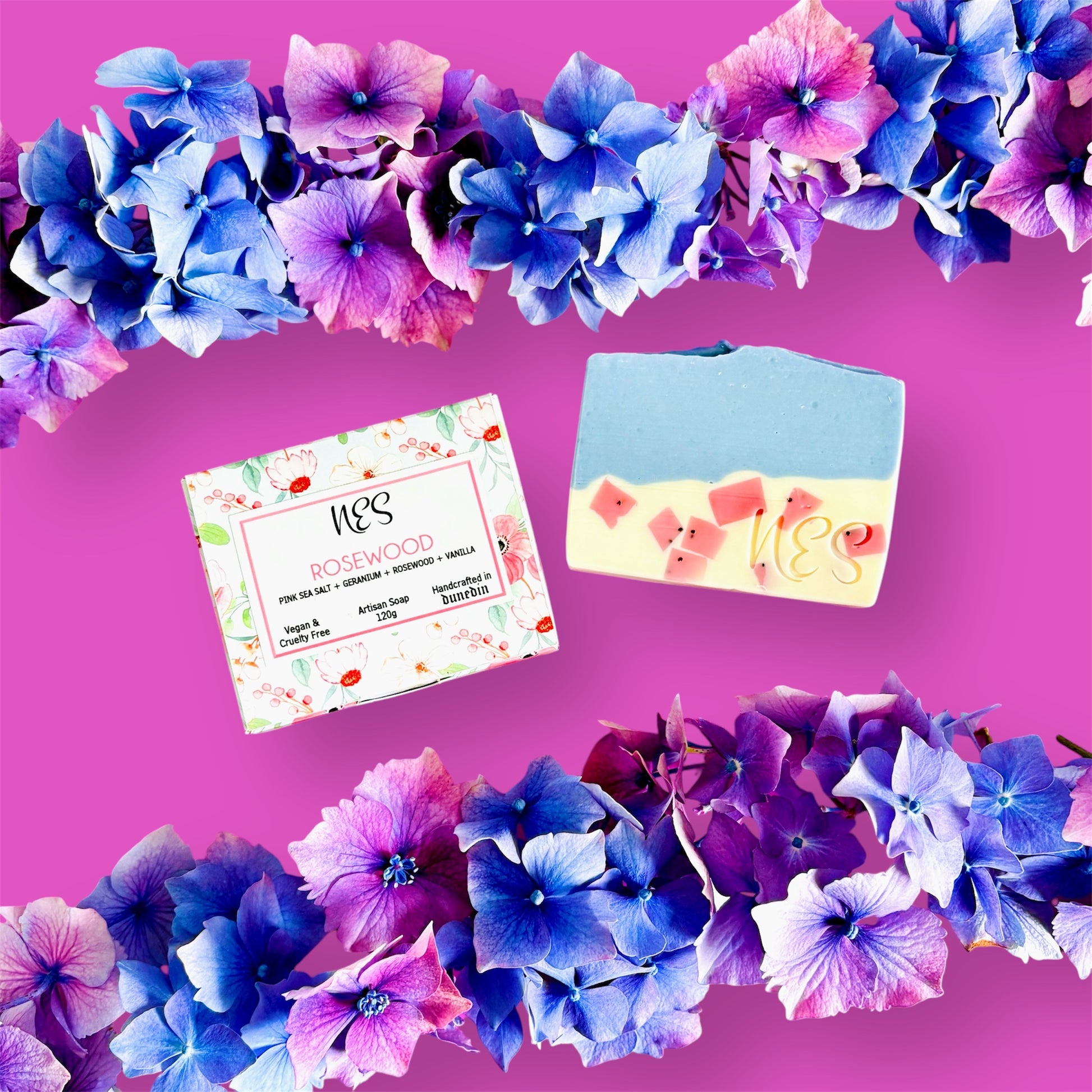 NES Rosewood artisan soap with pink sea salt, geranium, rosewood, and vanilla – handcrafted, vegan, and cruelty-free from NES Soap NZ. Styled with vibrant blue and purple hydrangeas on a pink background.